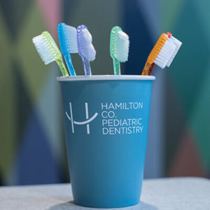 Colorful toothbrushes inside a mug with the hamilton County Pediatric Dentistry logo on it.