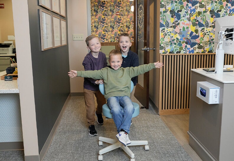 3 boys in a dentists office pushing a rolling chair
